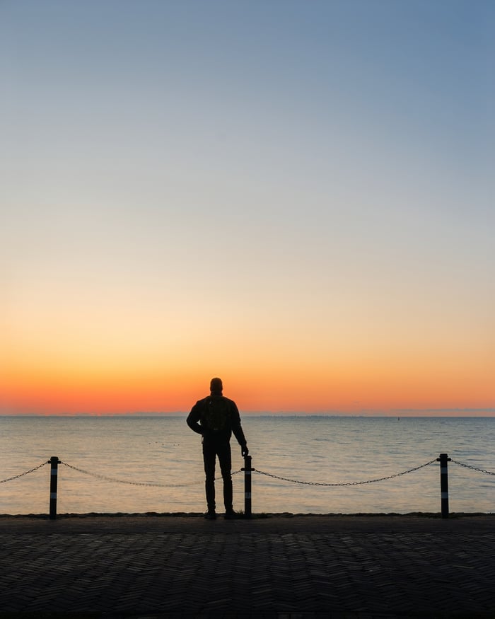 Een silhouet kijkt bij het eerste licht uit over zee, staand tussen twee palen met een ketting.