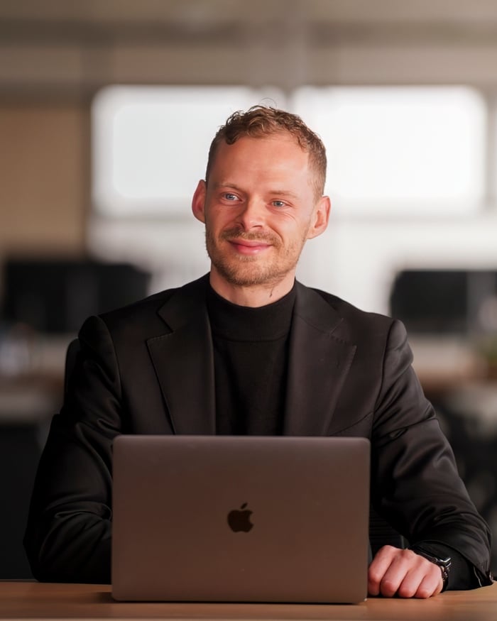 Robin Visser in a black suit and turtleneck behind a laptop in a bright office.
