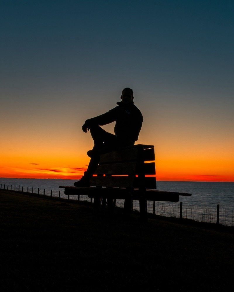 Silhouet van Robin op een bank aan de dijk bij zonsondergang boven het wad.